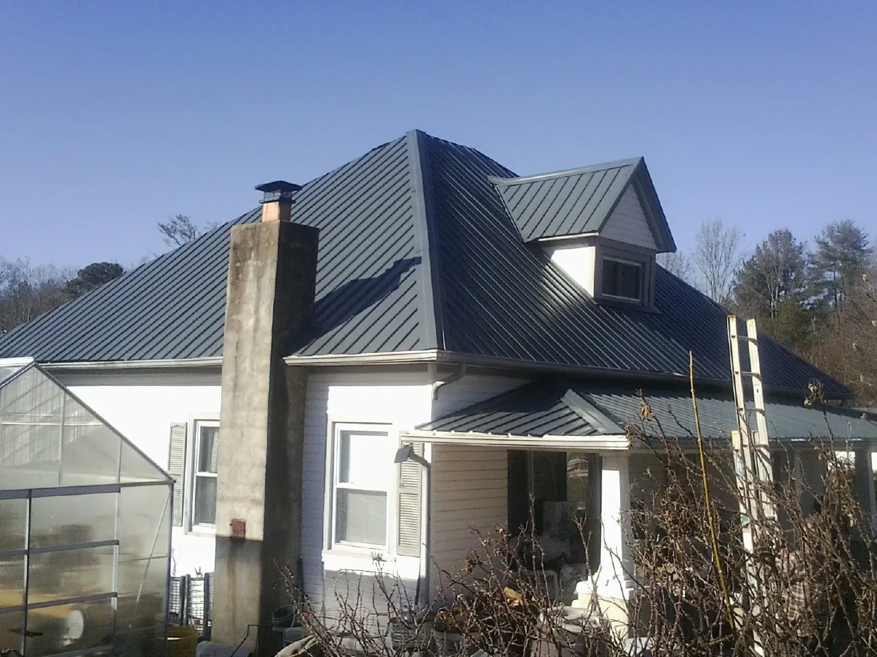 Dark blue standing seam metal roof on a white farmhouse with dormer — Slate & Tile Roof Repair by Roofing Brothers in Dane