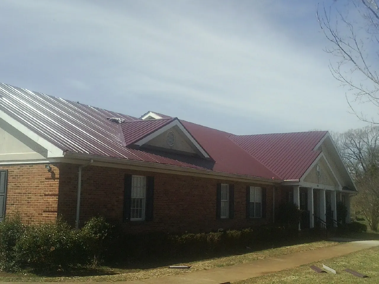 Red metal roof with gabled entries on a long brick building, from a Hail Damage Roof Repair job in Dane