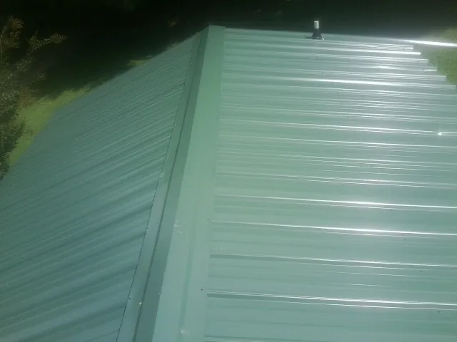 New green metal panels meeting at the ridge of a roof — Flat Roof Repair work by our crew in Dane