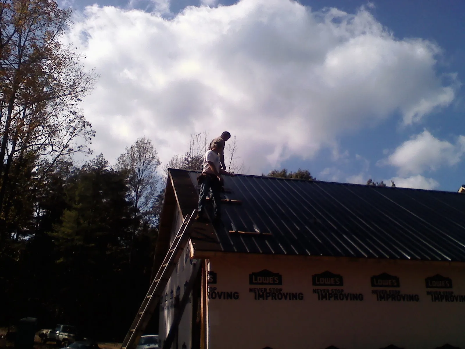 Roofer fastening dark metal panels high against a cloudy sky, from a Roof Inspection job in Dane