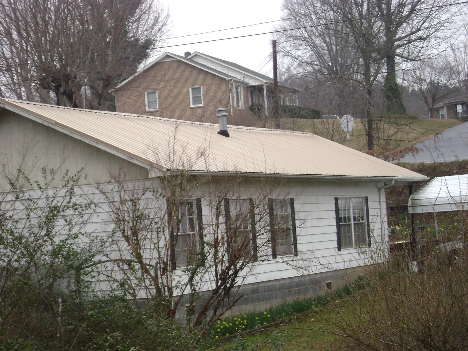 Tan metal roof on a white sided house set into a hillside — Commercial Roofing by Roofing Brothers in Dane